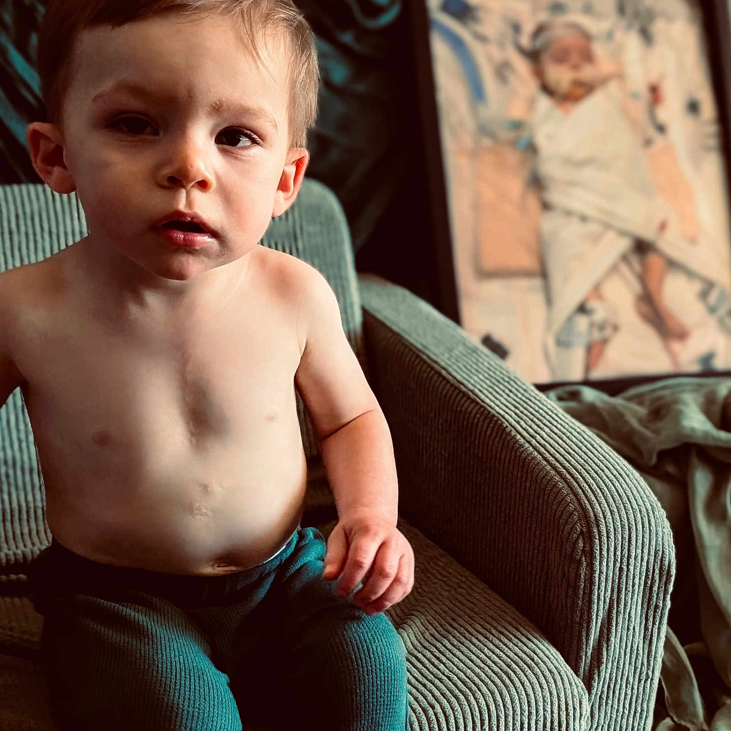 Arison is registered to the contest to win money with this photo: armchair, baby, blanket, boy, carpet, casual, child, cozy, curious, expression, frame, furniture, green, home, indoor, painting, portrait, seated, shirtless, toddler