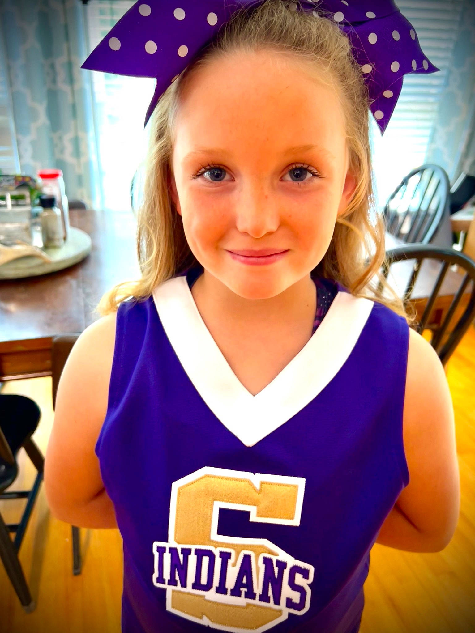 Braylie is registered to the contest to win money with this photo: blue, chair, cheerleading_uniform, clothing, electric_blue, face, fun, hairstyle, happy, jersey, joy, person, player, sleeve, smile, sports_jersey, sports_uniform, sportswear, t_shirt, toddler