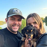 Apy participe au concours pour gagner de l'argent avec cette photo : man, woman, puppy, dog, smiling, outdoor, nature, lake, trees, sky, leash, cap, black_shirt, long_hair, happy, portrait, holding, pets, couple, sunlight