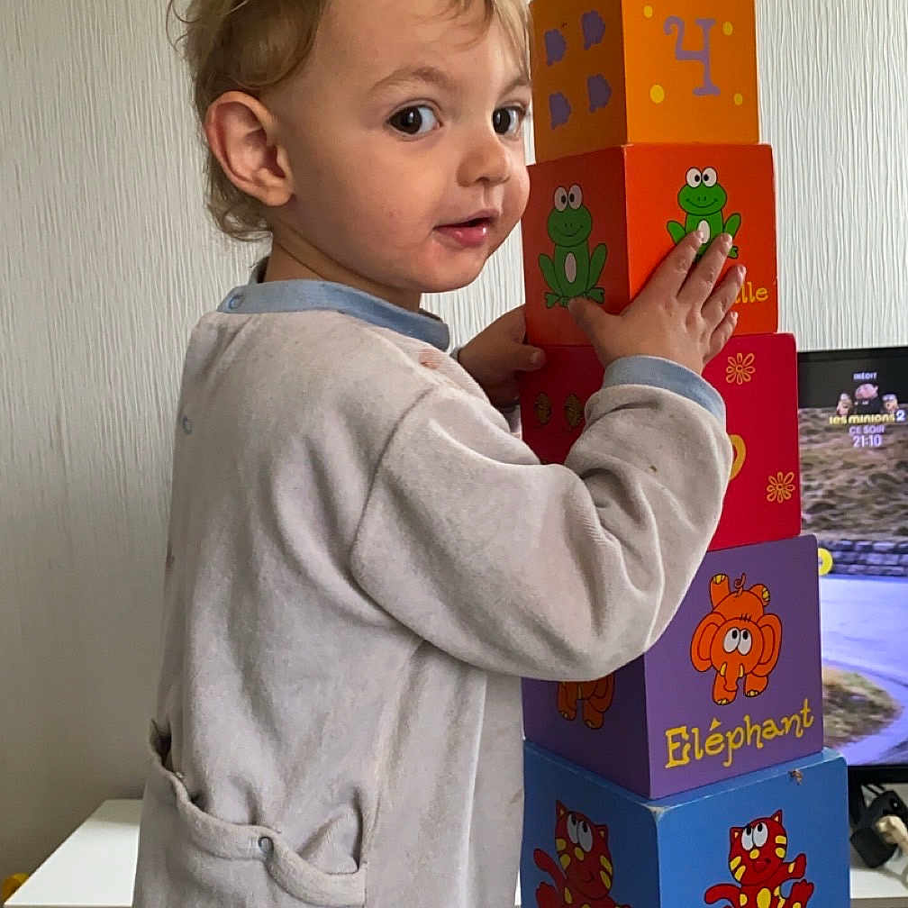 Maël participe au concours pour gagner de l'argent avec cette photo : baby, bodypart, bookcase, box, face, finger, furniture, hand, head, indoors, legoset, number, person, photoframe, photography, portrait, shelf, symbol, text, toy