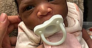Niyani is registered to the contest to win money with this photo: baby, newborn, pacifier, infant, pink_clothing, mittens, hand, closeup, portrait, face, skin, towel, curious, person, young_child, indoors, soft_lighting, cute, human, newborn_clothing