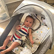 Jamiel is registered to the contest to win money with this photo: baby, infant, bassinet, striped_clothing, child, indoor, floor, fabric, pattern, mattress, toy, comfort, relaxing, cute, person, face, sleeping_area, baby_gear, foot, hand