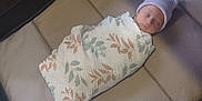 Loretta is registered to the contest to win money with this photo: baby, sleeping, swaddle, hat, cushion, playpen, crib, infant, peaceful, resting, soft, striped_hat, floral_pattern, blanket, indoors, child, newborn, comfort, cozy, quiet