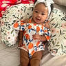 baby, child, infant, smiling, headband, bow, floral, pillow, blanket, bed, colorful_clothing, orange, blue, white, cute, indoors, person, portrait, happy, relaxed