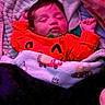 baby, infant, sleeping, portrait, face, red_outfit, blanket, wrapped, indoors, cozy, peaceful, closed_eyes, newborn, lying_down, bedding, colorful, pink_lighting, purple_lighting, cute, photography