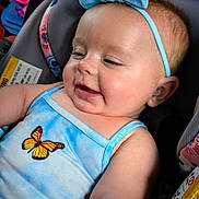 Enola is registered to the contest to win money with this photo: baby, child, blue_headband, bow, car_seat, smiling, happy, butterfly, clothing, infant, cute, portrait, closeup, skin, face, seatbelt, indoor, child_seat, head, person