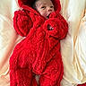 baby, infant, red_onesie, fluffy_clothing, hooded_outfit, blanket, bed, cute, newborn, child, face, sleepwear, soft_texture, cozy, lying_down, warm_clothing, indoors, portrait, small_hands, baby_clothes