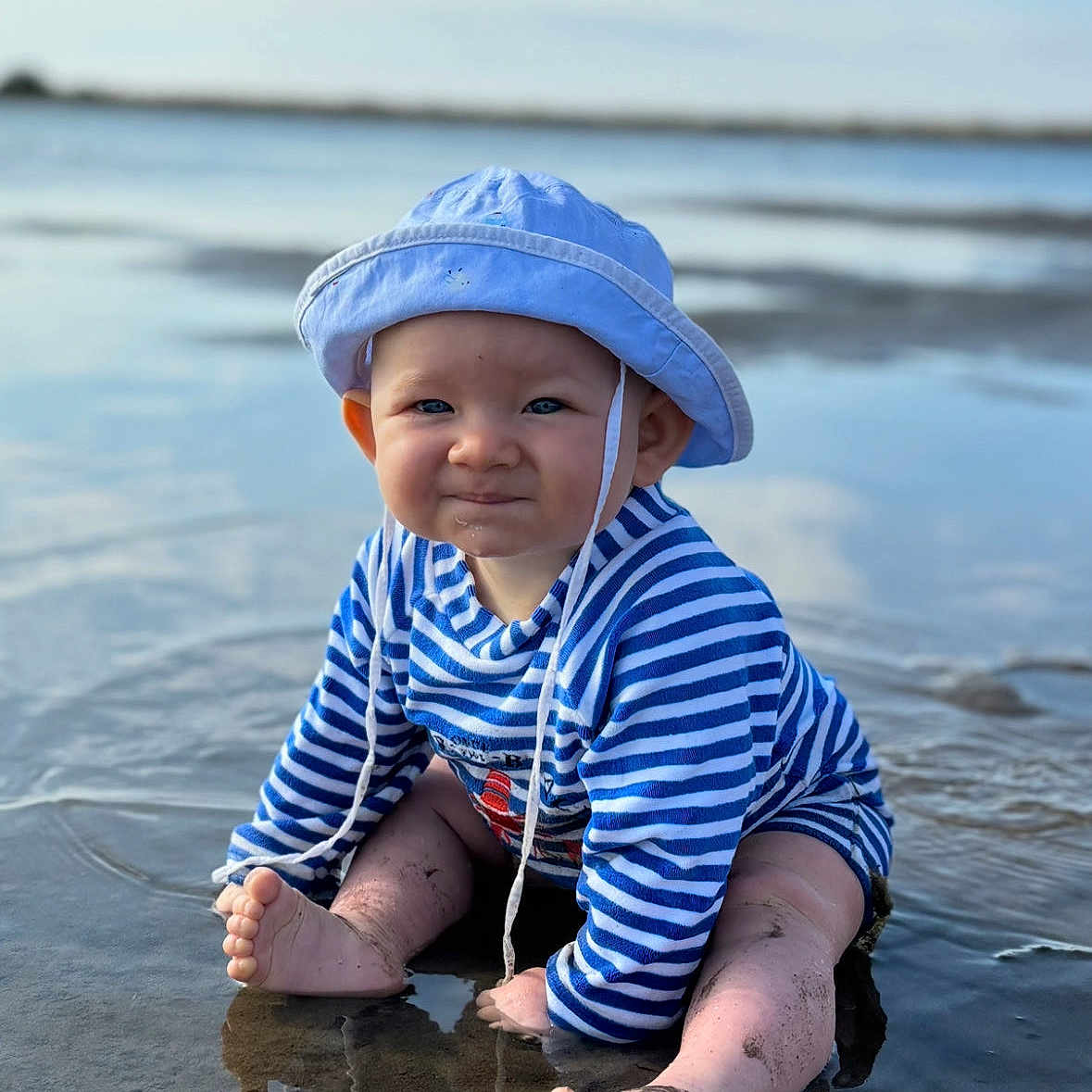 Lowen participe au concours pour gagner de l'argent avec cette photo : baby, child, beach, water, sand, hat, blue_stripes, sun_hat, sitting, reflection, smile, barefoot, outdoor, summer, cute, infant, ocean, playful, sunny, shallow_water