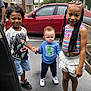 child, children, smiling, holding_hands, parking_lot, car, red_car, building, apartment, outdoor, casual_clothing, shorts, skirt, sneakers, braids, happy, group, people, daytime, asphalt