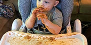 Ashton joined the competition — help win amazing prizes! toddler, child, high_chair, messy, food, sauce, face, hands, blue_eyes, gray_shirt, couch, purse, living_room, baby_food, tray, hair, indoor, seat, expression, young_child