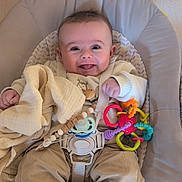 Maël a rejoint le concours — aidez-le/la à gagner de superbes lots ! baby, infant, smile, tongue_out, bouncer, toy_ring, pacifier, blanket, buckle, strap, onesie, pants, socks, cushion, chair, indoor, wall, close_up, happy, portrait