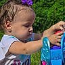 toddler, child, purple_bow, playing, toy, disney_princess, outdoor, greenery, sunlight, white_shirt, hands, face, profile, summer, young_child, plastic_toy, concentration, cute, small_hands, nature