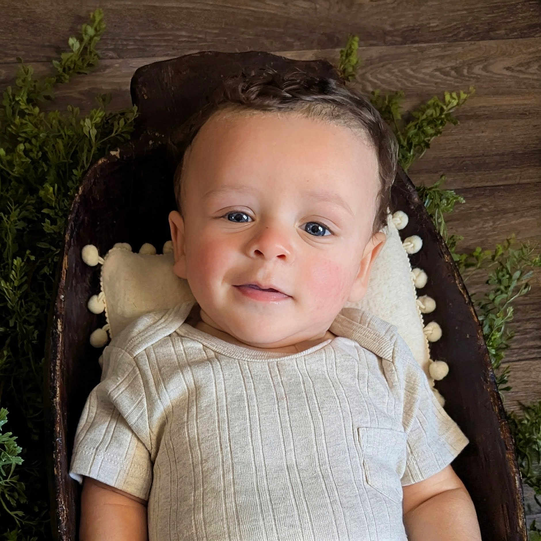 Scheffen is registered to the contest to win money with this photo: baby, child, face, smile, blue_eyes, curly_hair, wooden_bowl, pillow, greenery, wood_floor, cozy, portrait, indoor, cute, infant, clothing, short_sleeve, relaxed, skin, person