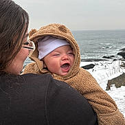 Ryder joined the competition — help win amazing prizes! baby, child, woman, glasses, ocean, snow, winter_clothing, hoodie, smile, outdoor, coastline, cold_weather, happy, person, face, water, nature, rock, sky, holding