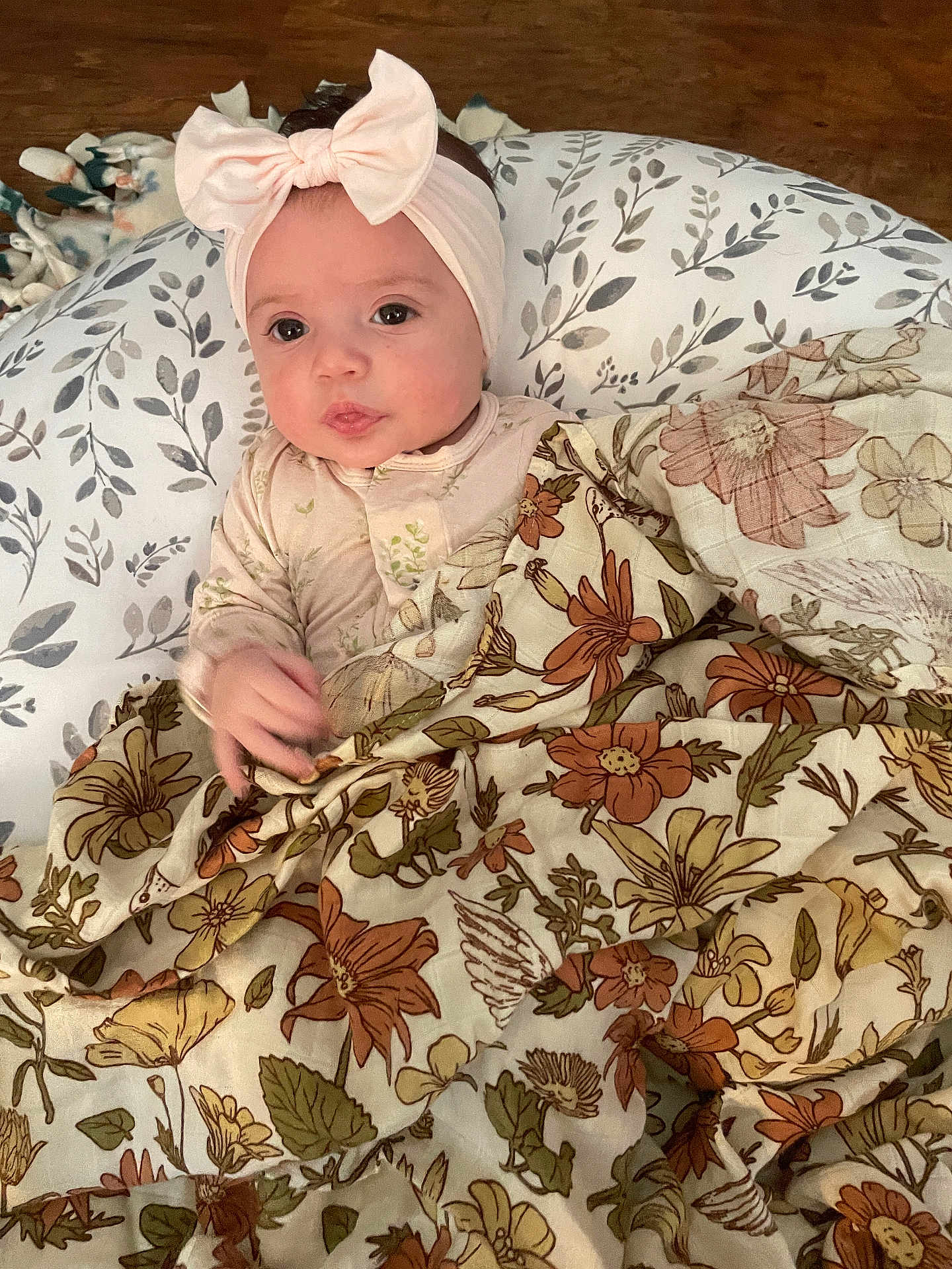 Tatum joined the competition — help win amazing prizes! baby, headband, bow, blanket, floral_pattern, pillow, wooden_floor, infant, cute, curious, face, person, indoors, child, clothing, soft_texture, laying, resting, young_child, cozy