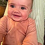 Tatum is registered to the contest to win money with this photo: baby, smiling, face, infant, child, happy, cozy, clothing, peach_outfit, cushion, striped, indoor, portrait, cute, skin, eyes, joy, seated, warm, closeup