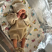 Noah is registered to the contest to win money with this photo: newborn, baby, infant, knitwear, hat, booties, yawning, hospital, bassinet, blanket, floral_pattern, sleeping, cozy, cute, child, person, indoor, soft_lighting, warm_colors, small_feet