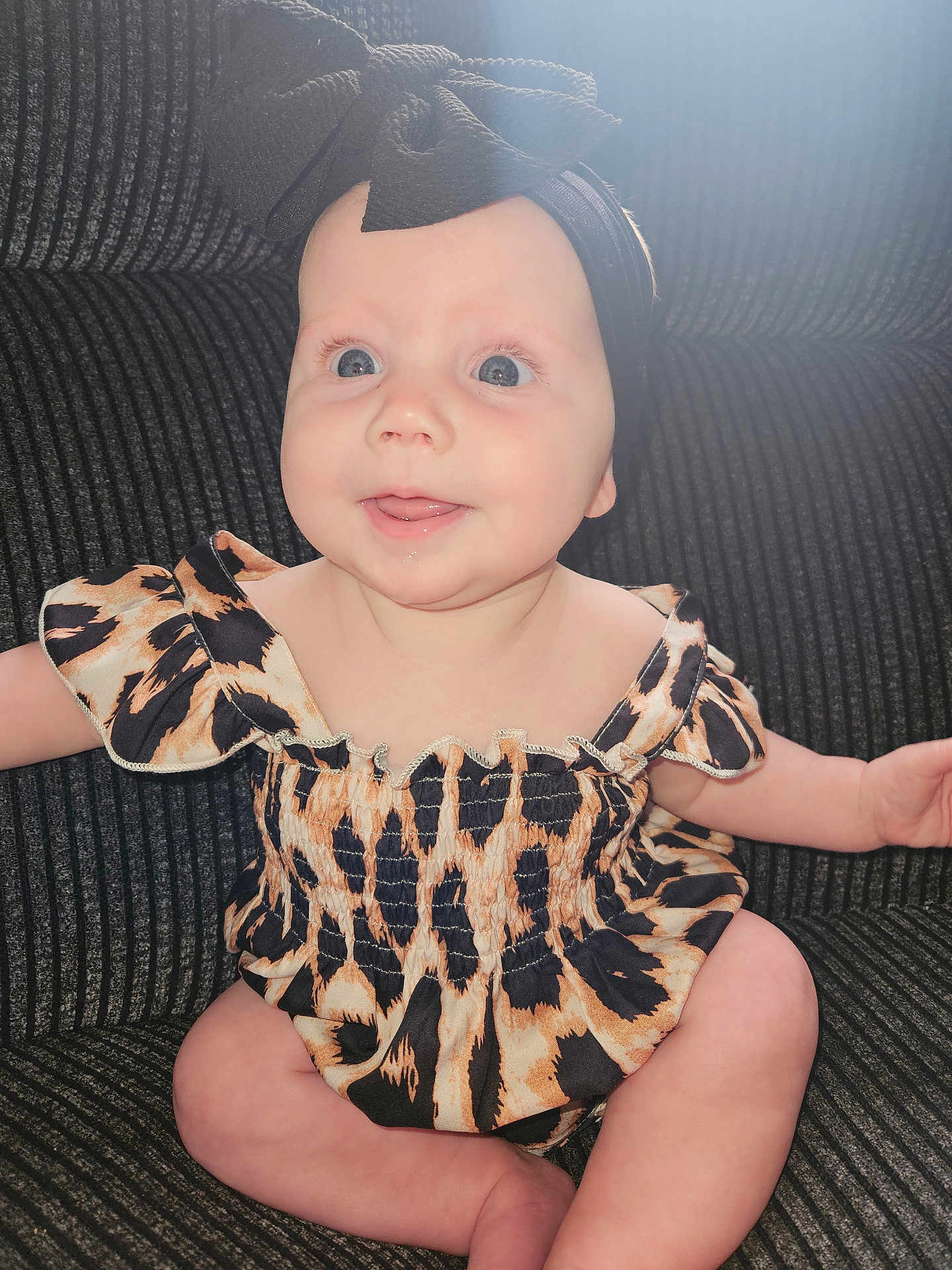 Calliope joined the competition — help win amazing prizes! baby, infant, child, smiling, headband, bow, leopard_print, dress, sitting, couch, indoor, cute, happy, blue_eyes, drool, skin, portrait, person, apparel, fabric