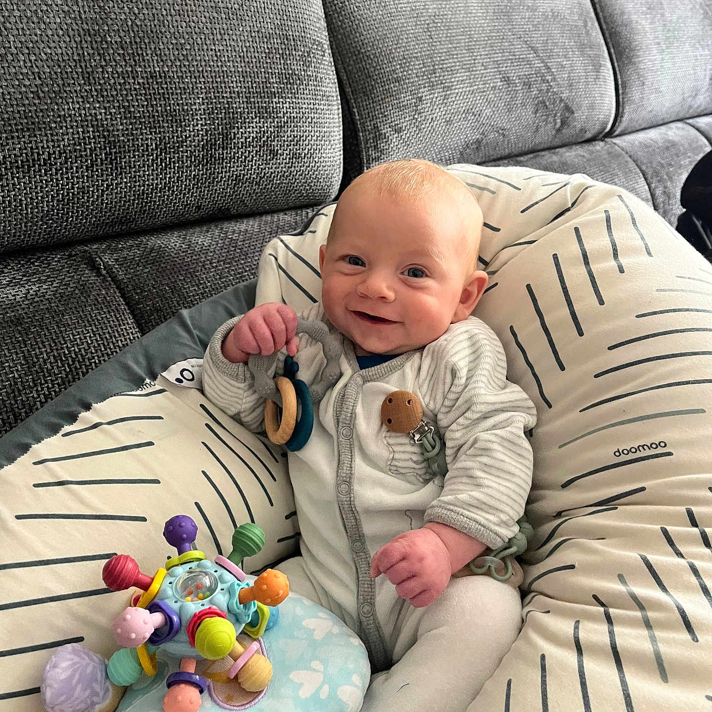 Aaron a rejoint le concours — aidez-le/la à gagner de superbes lots ! baby, smiling, toy, cushion, couch, infant, clothing, happy, indoor, person, face, hand, plush_toy, pattern, fabric, seated, cute, child, relaxing, home