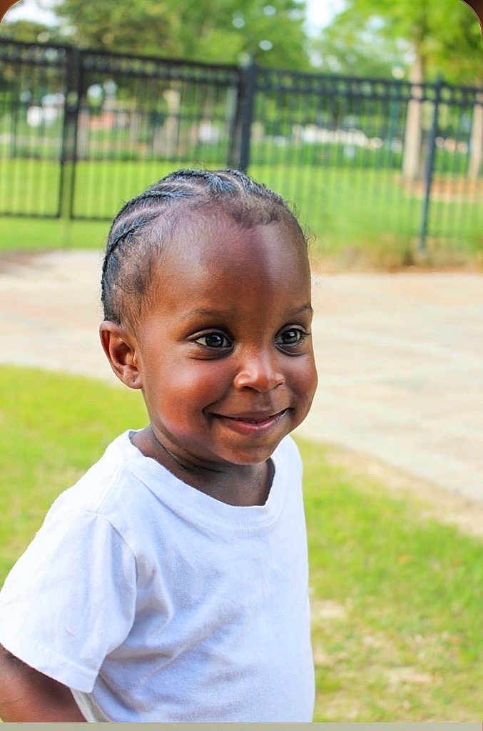 Brenynn joined the competition — help win amazing prizes! child, toddler, smiling, braided_hair, white_tshirt, outdoor, grass, fence, happy, portrait, person, cute, young, head, face, eyes, standing, sunlight, park, casual_clothing