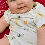 River is registered to the contest to win money with this photo: baby, infant, child, onesie, animal_print, giraffe, lion, zebra, cushion, red_background, smile, cute, chubby_cheeks, relaxed, indoors, portrait, skin, hand, face, happy