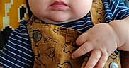 River is registered to the contest to win money with this photo: baby, child, blue_eyes, overalls, striped_shirt, dinosaur_print, hand, face, cheeks, person, indoor, couch, leather, clothing, cute, portrait, sitting, infant, young_child, casual