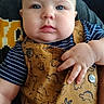 baby, child, blue_eyes, overalls, striped_shirt, dinosaur_print, hand, face, cheeks, person, indoor, couch, leather, clothing, cute, portrait, sitting, infant, young_child, casual