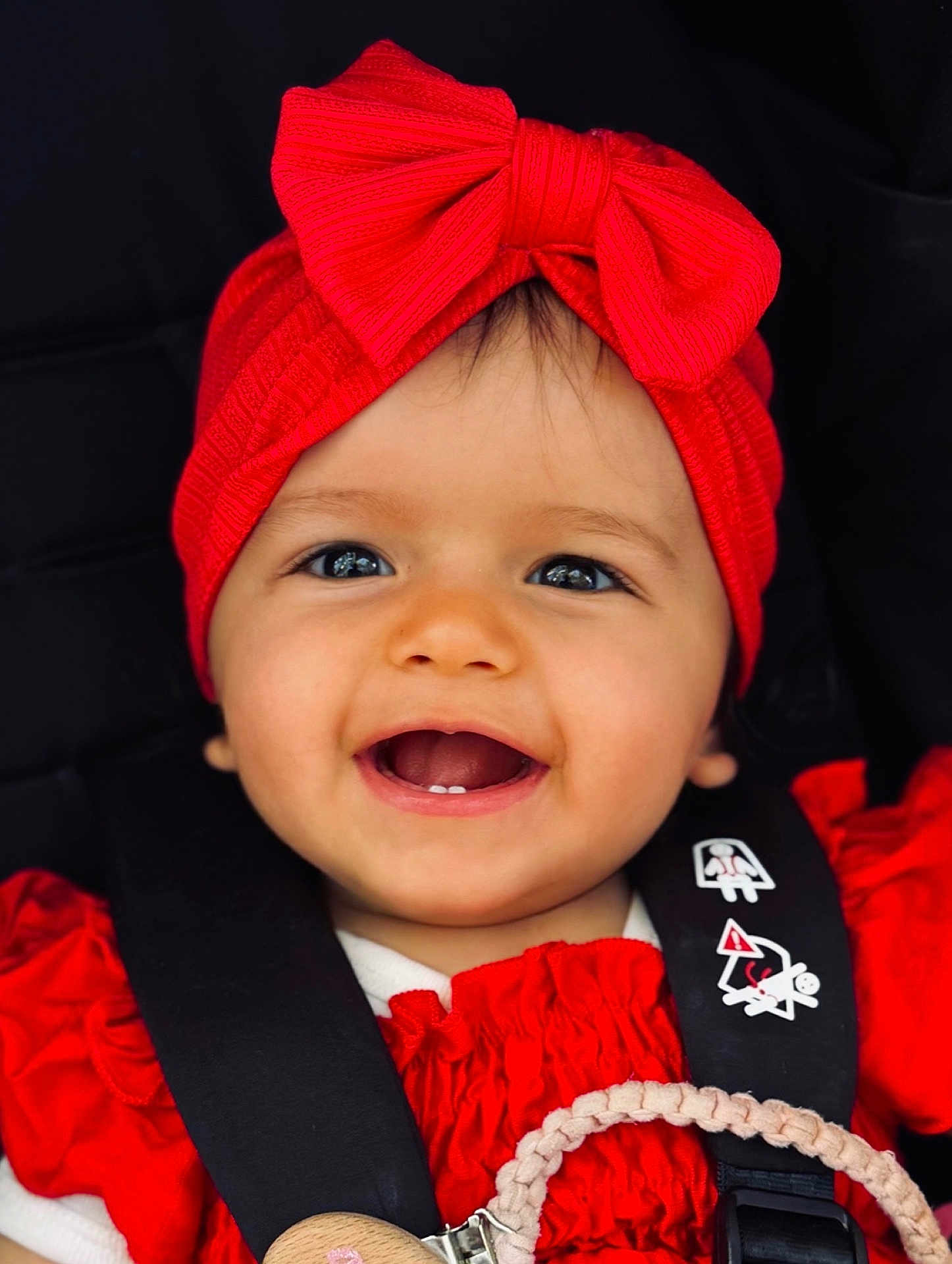 Ania a rejoint le concours — aidez-le/la à gagner de superbes lots ! baby, child, smiling, red_headband, red_bow, red_clothing, car_seat, black_straps, face, happy, teeth, infant, cute, closeup, portrait, person, baby_girl, headwear, accessory, safety