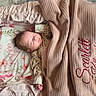 baby, bedding, blanket, close_up, clothing, cozy, embroidered_text, face, floral, indoors, infant, newborn, nursery, peaceful, photography, pink, portrait, relaxed, sleeping, swaddle