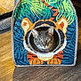 cat, pet_tent, tiger_design, gray_cat, indoor, wood_floor, animal, pet, curious, face, colorful, fabric, home, cozy, playful, whiskers, ears, sitting, cute, domestic_cat
