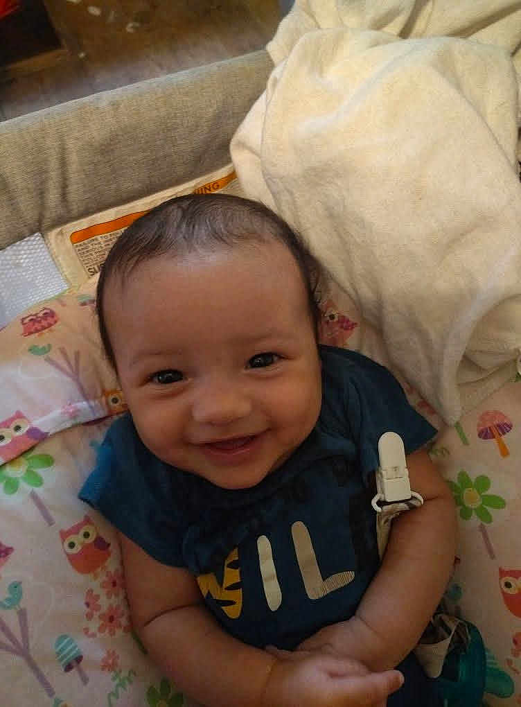 Elijah is registered to the contest to win money with this photo: baby, smiling, infant, blue_shirt, cushion, blanket, owl_pattern, indoor, happy, cute, child, person, seated, comfort, soft_toy, fabric, clothing, face, head, skin