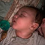 baby, sleeping, pacifier, clothing, gray_shirt, patterned_bedding, face, head, ear, infant, closeup, resting, peaceful, indoors, child, person, soft_light, cute, newborn, young_child