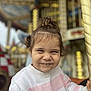 child, toddler, smile, gap_tooth, portrait, carousel, amusement_park, ride, hair_bun, sweater, pink_and_white, striped_sweater, happy, face, hand, pole, bokeh, outdoor, cute, photography