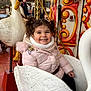 child, toddler, girl, smile, carousel, swan, amusement_ride, pigtails, winter_coat, outdoor, seat, ornate_decoration, happy, playful, family, belt, wooden_floor, bell, person_in_background, portrait