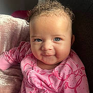 Ariana joined the competition — help win amazing prizes! baby, child, curly_hair, blue_eyes, pink_clothing, onesie, strawberry_pattern, smile, face, portrait, plush_blanket, soft_lighting, indoors, comfortable, cute, infant, happy, close_up, person, young