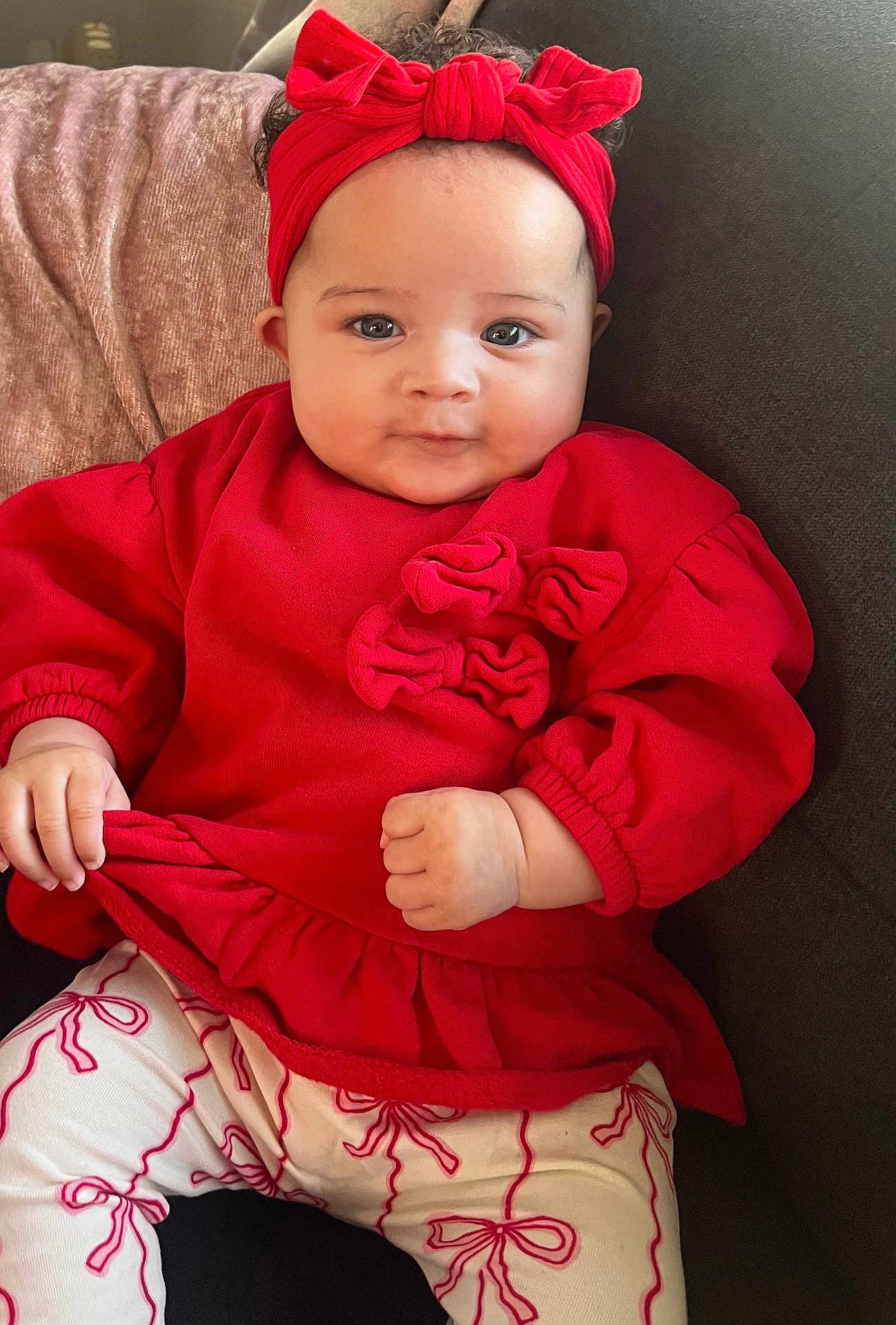 Ariana is registered to the contest to win money with this photo: baby, child, red_headband, red_top, white_leggings, bows, couch, indoor, cute, portrait, smiling, infant, clothing, hands, face, sitting, young_child, comfortable, fashion, adorable