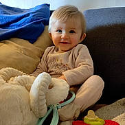 Kira a rejoint le concours — aidez-le/la à gagner de superbes lots ! toddler, child, smile, plush_toy, blanket, cushion, sofa, indoors, clothing, happy, cute, baby, play, comfort, soft_toys, face, person, home, relax, seated