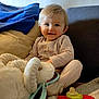 toddler, child, smile, plush_toy, blanket, cushion, sofa, indoors, clothing, happy, cute, baby, play, comfort, soft_toys, face, person, home, relax, seated
