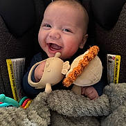 Lincoln is registered to the contest to win money with this photo: baby, infant, smiling, car_seat, blanket, plush_toy, teether, stuffed_animal, happy, portrait, closeup, hand, clothing, rosy_cheeks, buckle, headrest, soft_toy, cozy, plaything, seat_label