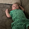 baby, infant, green_clothing, dinosaur_pattern, couch, pillow, indoor, relaxed, child, person, furniture, home, portrait, lying_down, casual, comfortable, young, cute, infant_clothing, expression