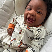 Azaiah joined the competition — help win amazing prizes! baby, child, infant, smiling, laughing, onesie, animal_print, curly_hair, cushion, soft_fabric, indoor, happy, cute, closeup, portrait, relaxed, cozy, person, seated, comfortable