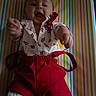 baby, child, smiling, reaching, red_shorts, white_shirt, patterned_clothing, striped_background, happy, playful, indoor, portrait, infant, cute, person, clothing, fabric, colorful, young_child, lying_down