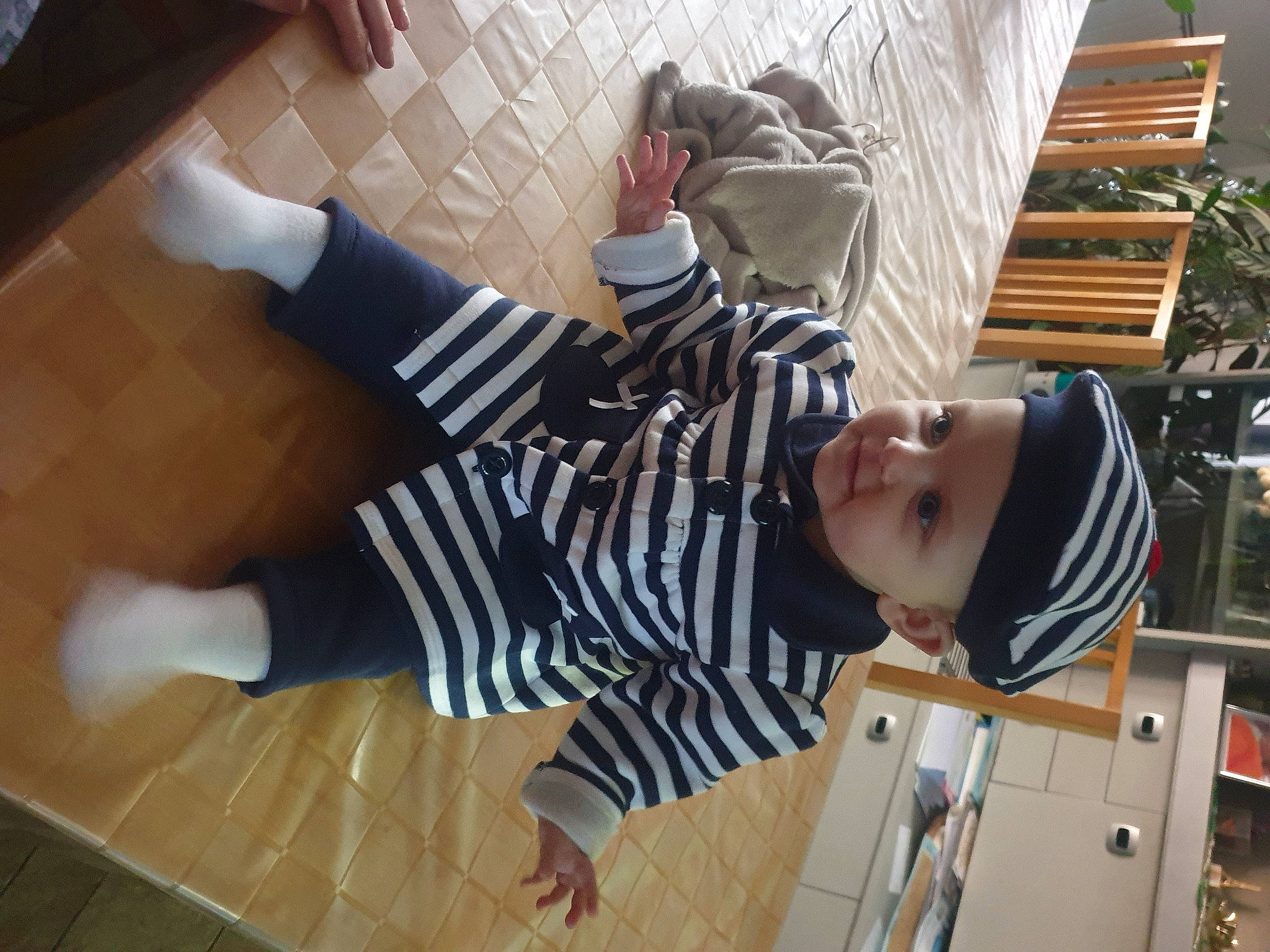 Léna a rejoint le concours — aidez-le/la à gagner de superbes lots ! baby_toddler_clothing, child, comfort, floor, flooring, hardwood, hat, headwear, houseplant, knee, pattern, person, plant, room, sleeve, sock, t_shirt, thigh, toddler, wood