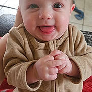 Timéo a rejoint le concours — aidez-le/la à gagner de superbes lots ! baby, infant, child, smiling, tongue_out, big_eyes, chubby_cheeks, hands, clothing, brown_onesie, close_up, portrait, indoor, tile_floor, blanket, seat, happy, cute, skin, head