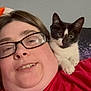 person, glasses, cat, kitten, black_and_white_cat, shoulder, red_shirt, indoor, closeup, face, pet, cute, curious, animal, portrait, casual, resting, human, friendship, companion