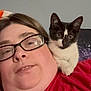 person, cat, kitten, glasses, red_shirt, shoulder, indoor, portrait, close_up, black_and_white_cat, curious, face, eyewear, casual, resting, pet, animal, companion, domestic, relaxed