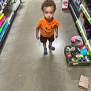 Tony Ray Jr is registered to the contest to win money with this photo: blue_socks, box, casual, child, childrens_clothing, concrete_floor, curiosity, curly_hair, floor_markings, indoor, looking_up, mixed_expression, orange_shirt, pumpkin_design, shelves, shopping, standing, store_aisle, toddler, toys