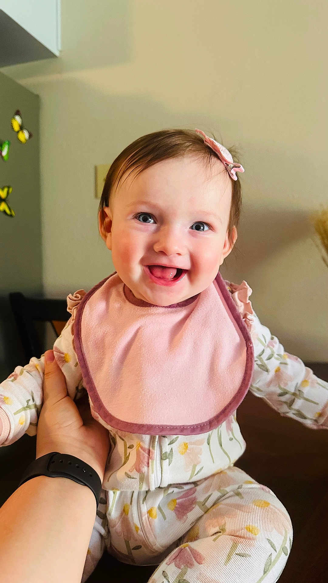 Abigail Aleksa is registered to the contest to win money with this photo: baby, infant, smiling, pink_bib, floral_pajamas, hand, smartwatch, indoor, butterfly_decorations, happy, child, cute, portrait, person, face, head, clothing, sitting, home, cheerful