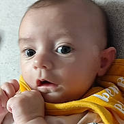 Adèle participe au concours pour gagner de l'argent avec cette photo : baby, close_up, face, eyes, infant, yellow_bib, hand, skin, cute, expression, portrait, child, person, soft_surface, clothing, young, indoors, human, head, curious