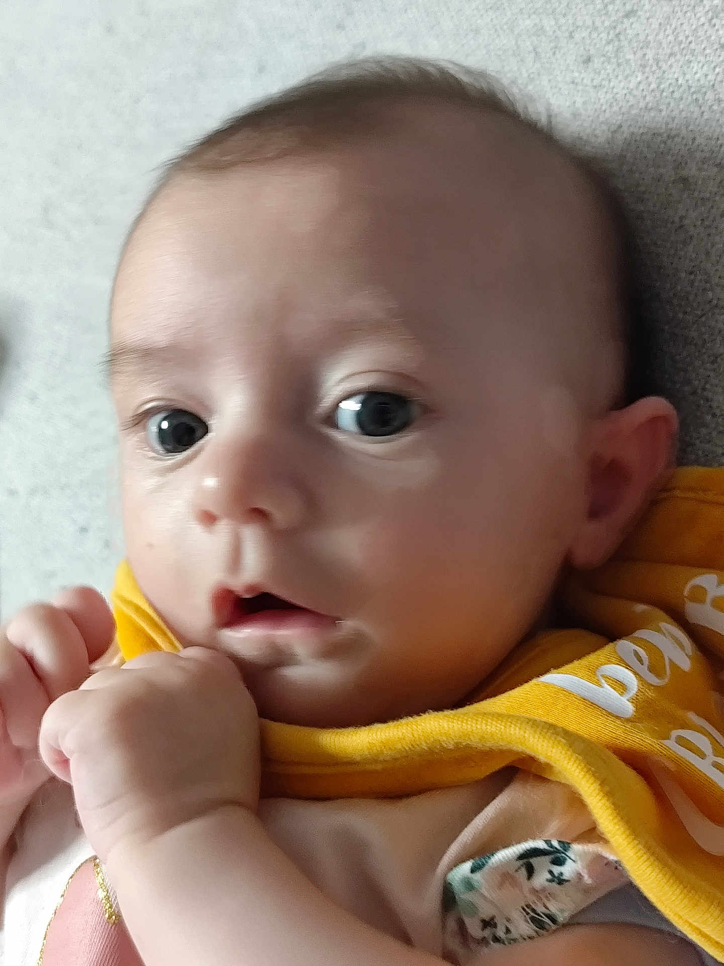 Adèle participe au concours pour gagner de l'argent avec cette photo : baby, close_up, face, eyes, infant, yellow_bib, hand, skin, cute, expression, portrait, child, person, soft_surface, clothing, young, indoors, human, head, curious